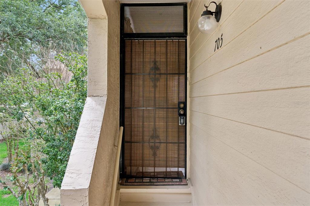 A beige exterior wall features a front door with a dark metal security screen — 3148 S SEMORAN BLVD UNIT 705, ORLANDO, FL
