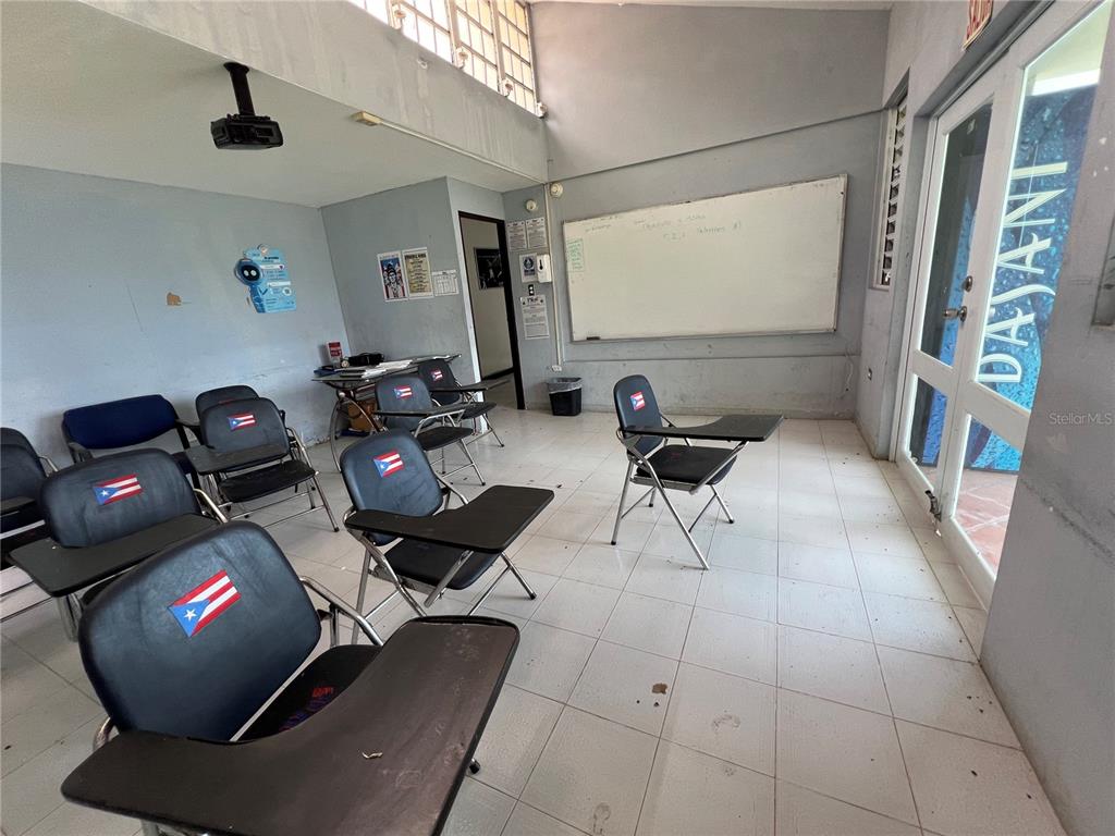 A classroom with tiled floors, a whiteboard, and several chairs with attached desks — Marginal PR-52 BARRIO MONTELLANOS, SECTOR PEPE HOYOS, CAYEY, PR