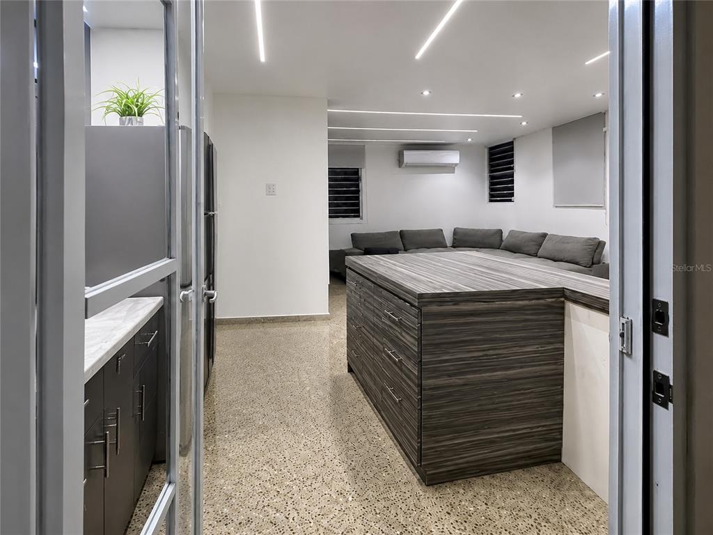 A kitchen with a large wood-grain island and dark cabinetry opens into a living area — . ESMERALDA UNIT E-12, SAN JUAN, PR