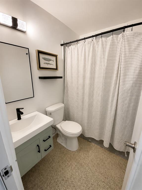 A bathroom features a sage green vanity, a white toilet, and a striped shower curtain — . ESMERALDA UNIT E-12, SAN JUAN, PR