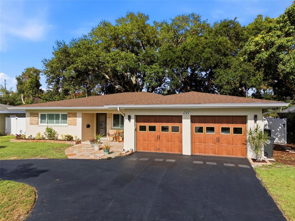 A single-story house with a two-car garage, stone patio, and large trees in the yard — 1727 CYPRESS AVENUE, BELLEAIR, FL