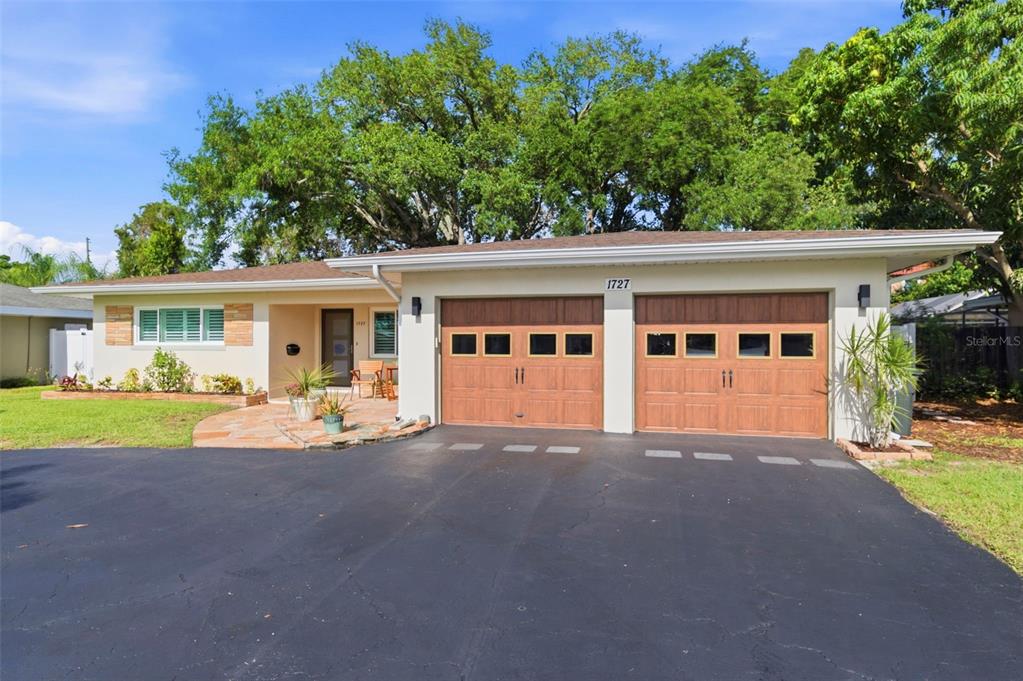 A single-story house with a curved asphalt driveway, two-car garage, and mature trees — 1727 CYPRESS AVENUE, BELLEAIR, FL