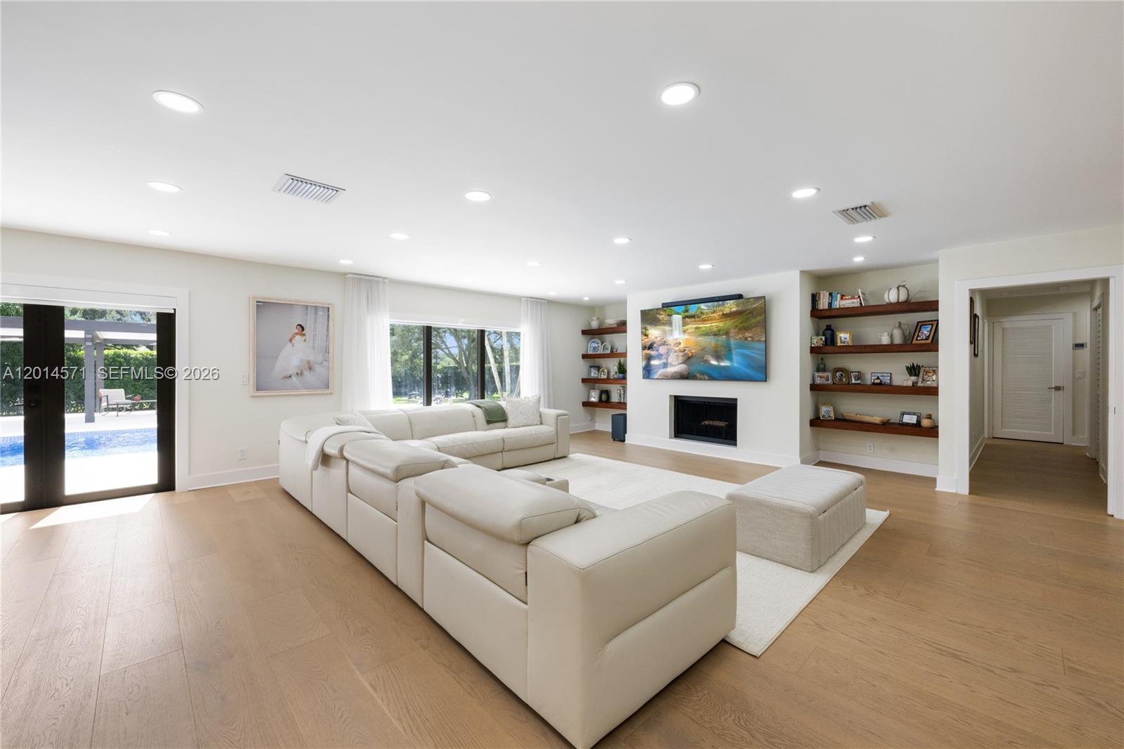 A bright living room features a large sectional sofa, a fireplace, and built-in wooden shelving — 15110 N Saxon Cir, Southwest Ranches FL 33331, SOUTHWEST RANCHES, FL