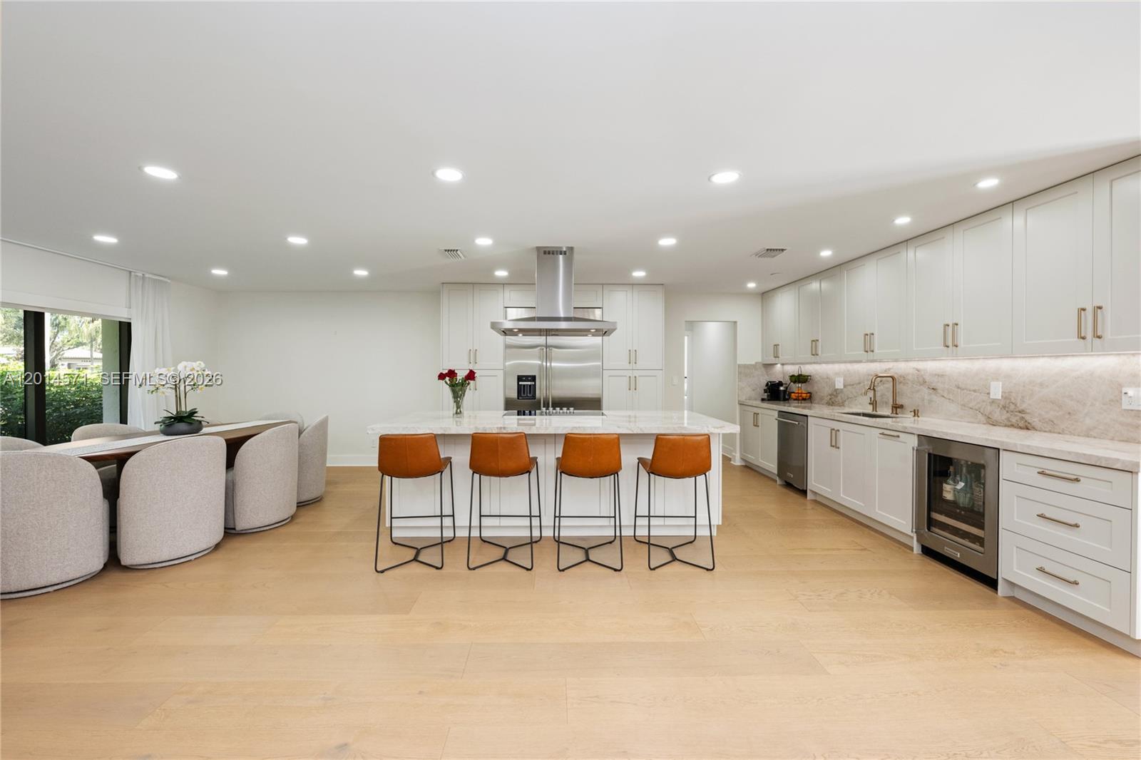 A modern kitchen features light wood floors, white cabinetry, a marble island, and bar stools — 15110 N Saxon Cir, Southwest Ranches FL 33331, SOUTHWEST RANCHES, FL