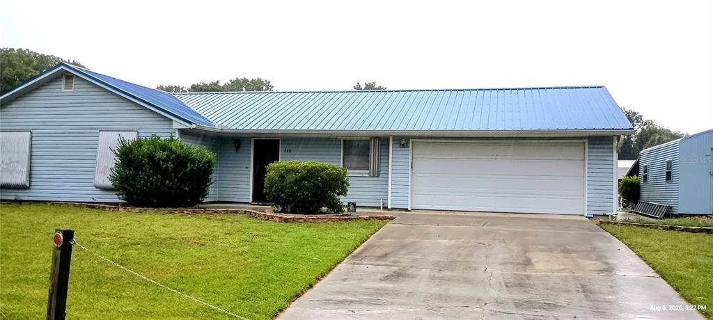 A single-story house with light blue siding, a blue metal roof, and a concrete driveway — 148 HICKS AVENUE, CRESCENT CITY, FL