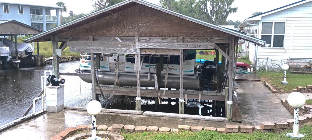 A pontoon boat sits on a lift under a wooden roof structure by a canal — 148 HICKS AVENUE, CRESCENT CITY, FL