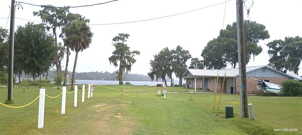 A grassy yard with a chain-link fence leads toward a lake and a brick house — 148 HICKS AVENUE, CRESCENT CITY, FL