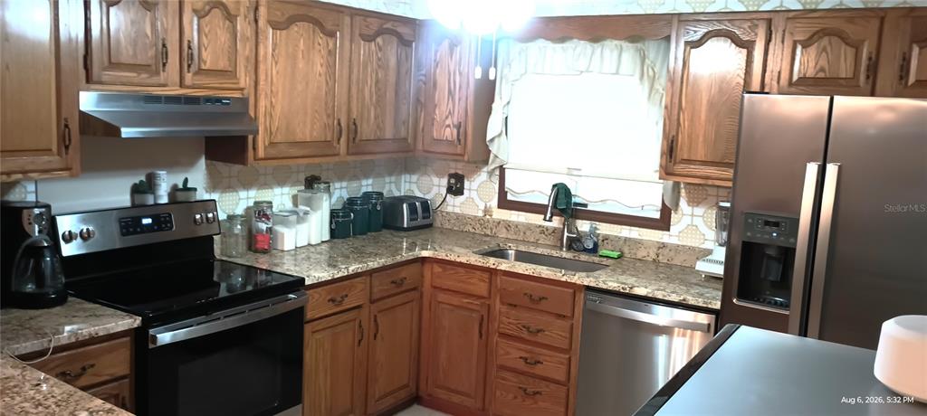 A kitchen features oak cabinets, granite countertops, stainless steel appliances, and a patterned tile backsplash — 148 HICKS AVENUE, CRESCENT CITY, FL
