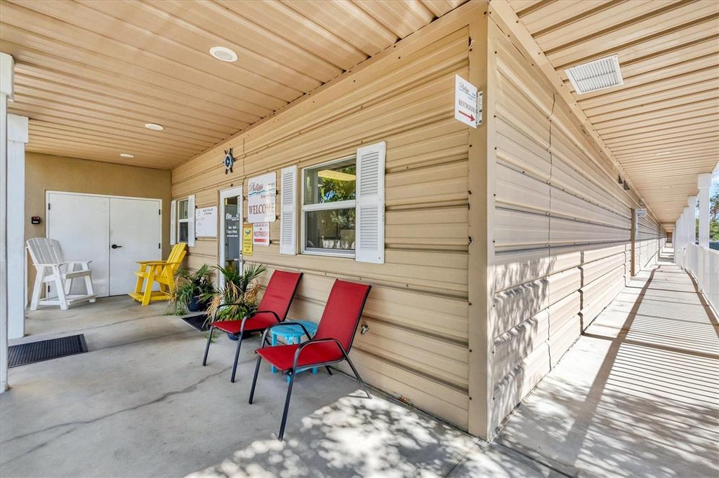 A covered exterior walkway features a beige metal building, red patio chairs, and seating — 1780 PHILLIPPI SHORES DRIVE UNIT E1-46, SARASOTA, FL