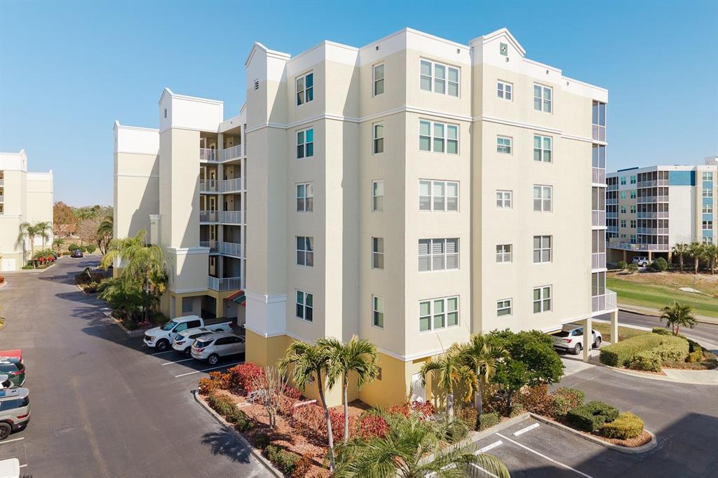 An exterior view of a multi-story beige apartment building with a parking lot and palm trees — 1200 COUNTRY CLUB DRIVE UNIT 4202, LARGO, FL