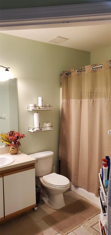 A bathroom features a vanity, a toilet, two wall-mounted shelves, and a tan shower curtain — 9517 AMBERDALE COURT UNIT 202, RIVERVIEW, FL
