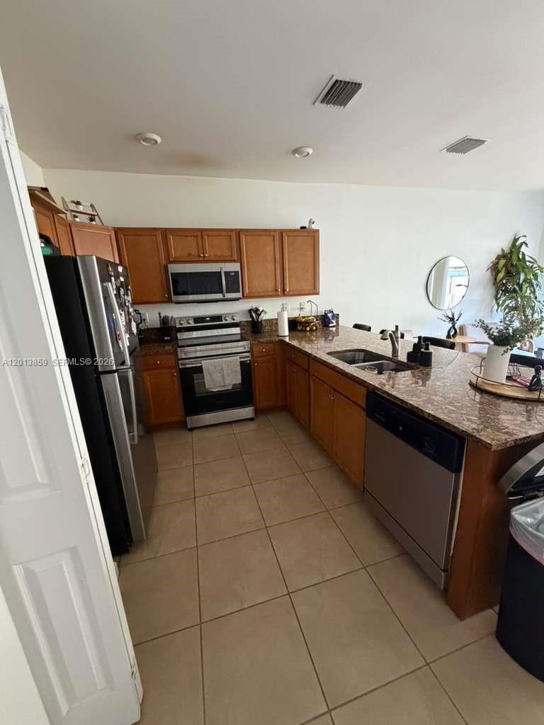 A kitchen features wood cabinets, granite countertops, stainless steel appliances, and beige tile flooring — 9337 W 33rd Way, Hialeah FL 33018, HIALEAH, FL