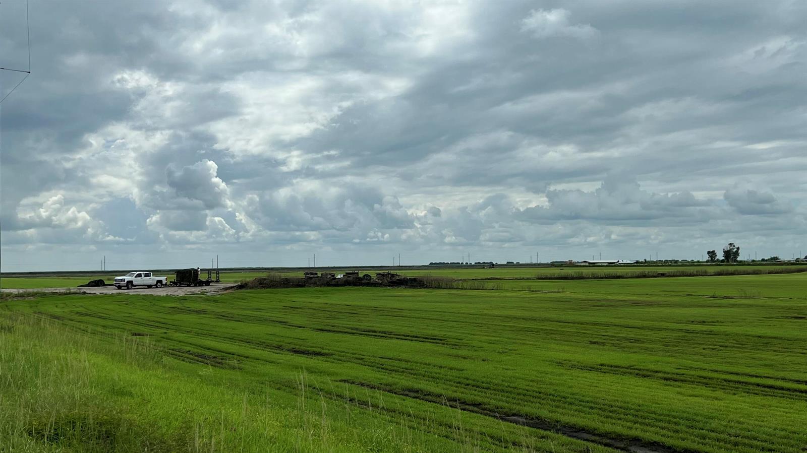 A white pickup truck with a trailer is parked on a gravel lot beside green fields — 400 State Road 80, Belle Glade FL 33430, BELLE GLADE, FL