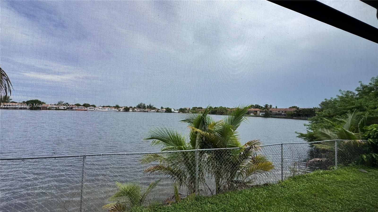 A view of a lake from behind a screened-in porch with a chain-link fence — 2531 W 60th Pl # 18, Hialeah FL 33016, HIALEAH, FL