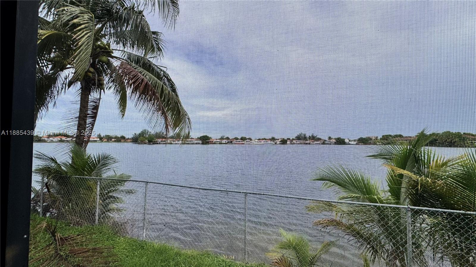 A view of a lake and palm trees seen through a screened-in porch enclosure — 2531 W 60th Pl # 18, Hialeah FL 33016, HIALEAH, FL