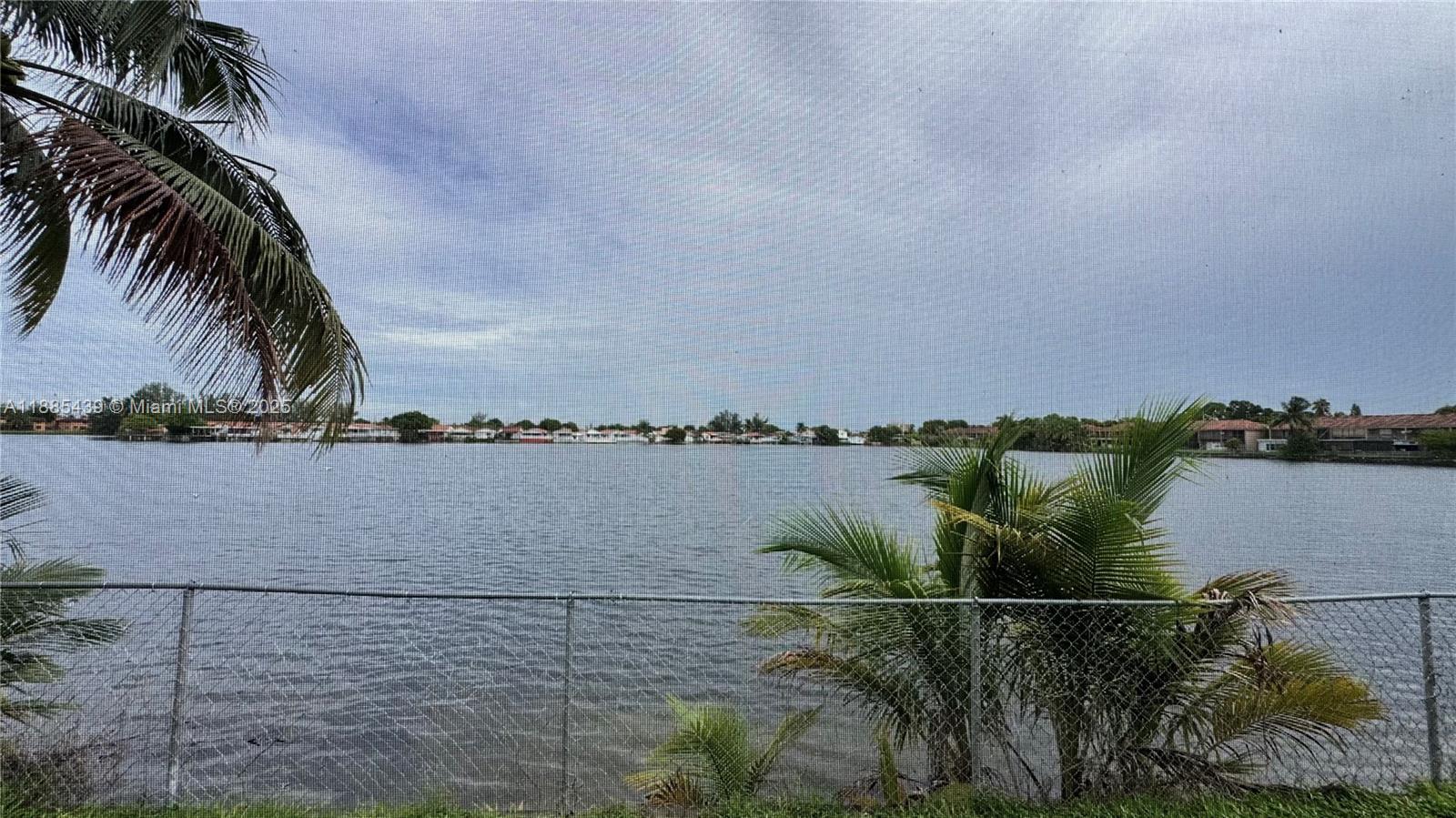 A view of a lake from behind a chain-link fence with palm trees — 2531 W 60th Pl # 18, Hialeah FL 33016, HIALEAH, FL