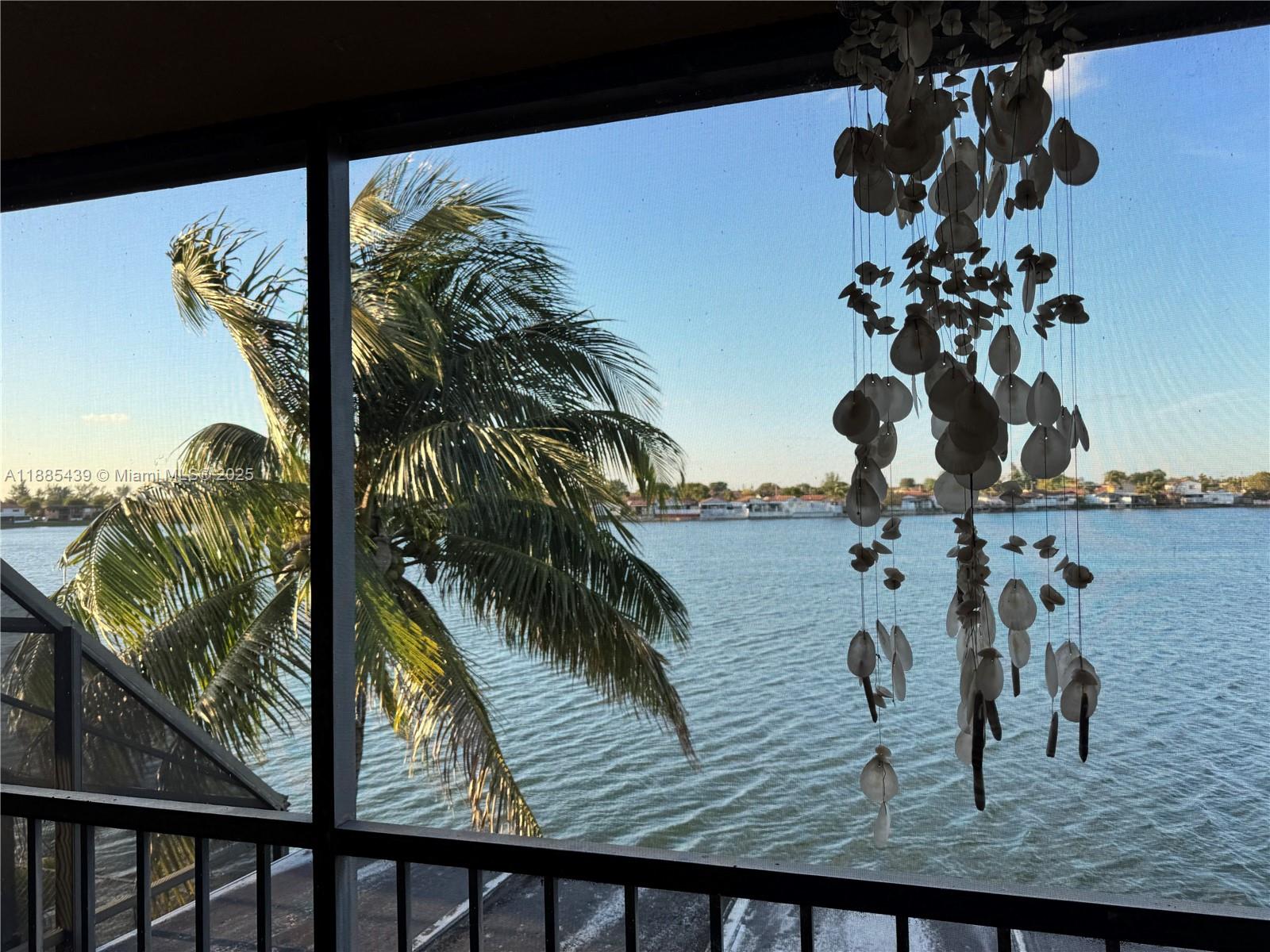 A view of a palm tree and water from a screened-in balcony with hanging shells — 2531 W 60th Pl # 18, Hialeah FL 33016, HIALEAH, FL
