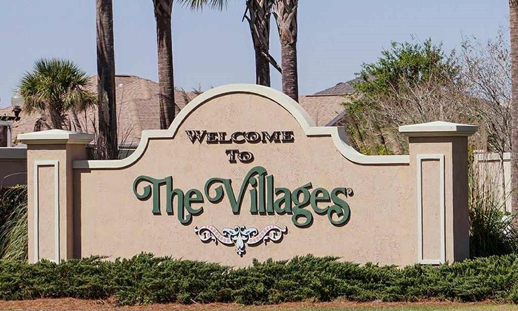 A beige stucco monument sign welcomes visitors to The Villages community with palm trees behind — 1370 SE 20TH TERRACE, SUMTERVILLE, FL