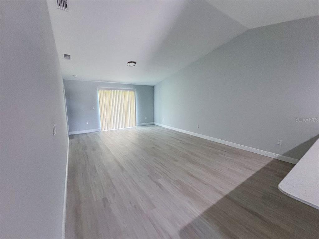 An empty living room features light gray walls, wood-look flooring, and a sliding glass door — 8373 AGATE STREET UNIT 8375, PORT CHARLOTTE, FL