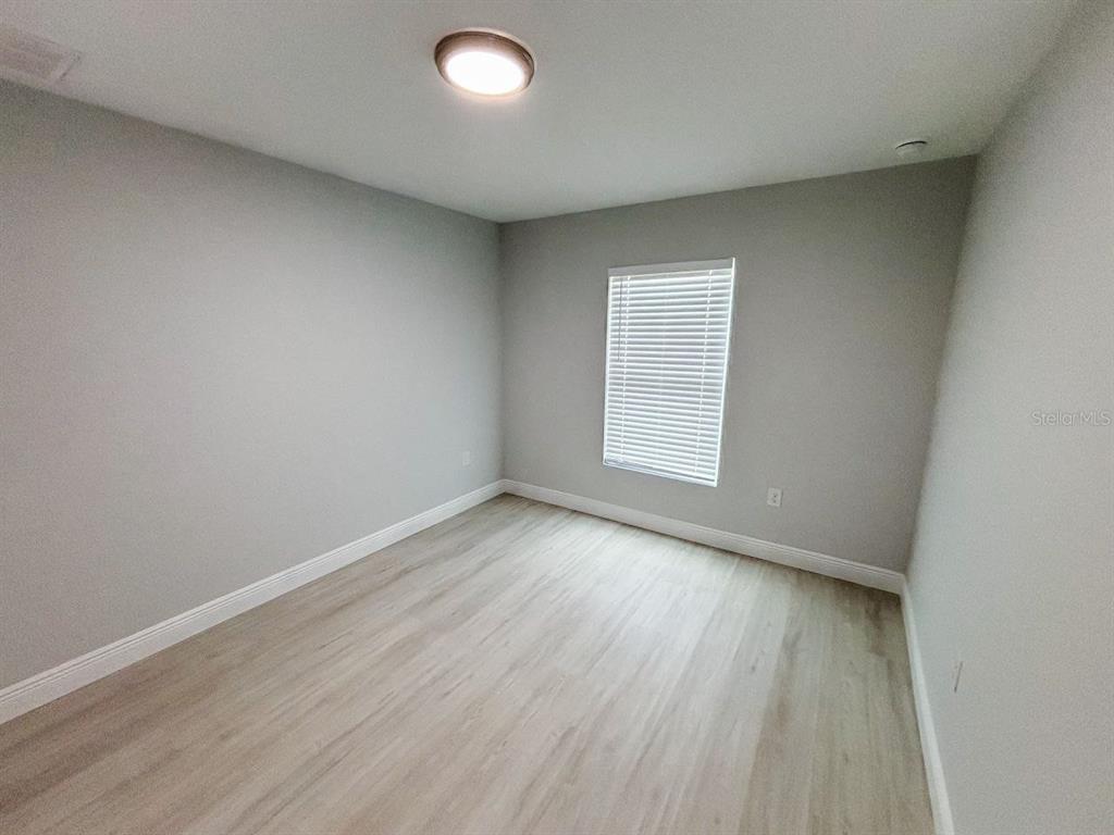 An empty room features light gray walls, wood-look flooring, a single window, and a ceiling light — 8373 AGATE STREET UNIT 8375, PORT CHARLOTTE, FL