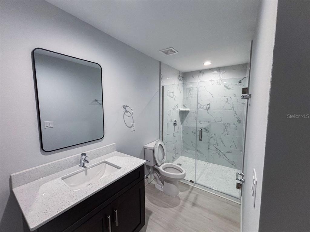 A modern bathroom features a dark vanity, a marble-tiled walk-in shower, and a toilet — 8373 AGATE STREET UNIT 8375, PORT CHARLOTTE, FL