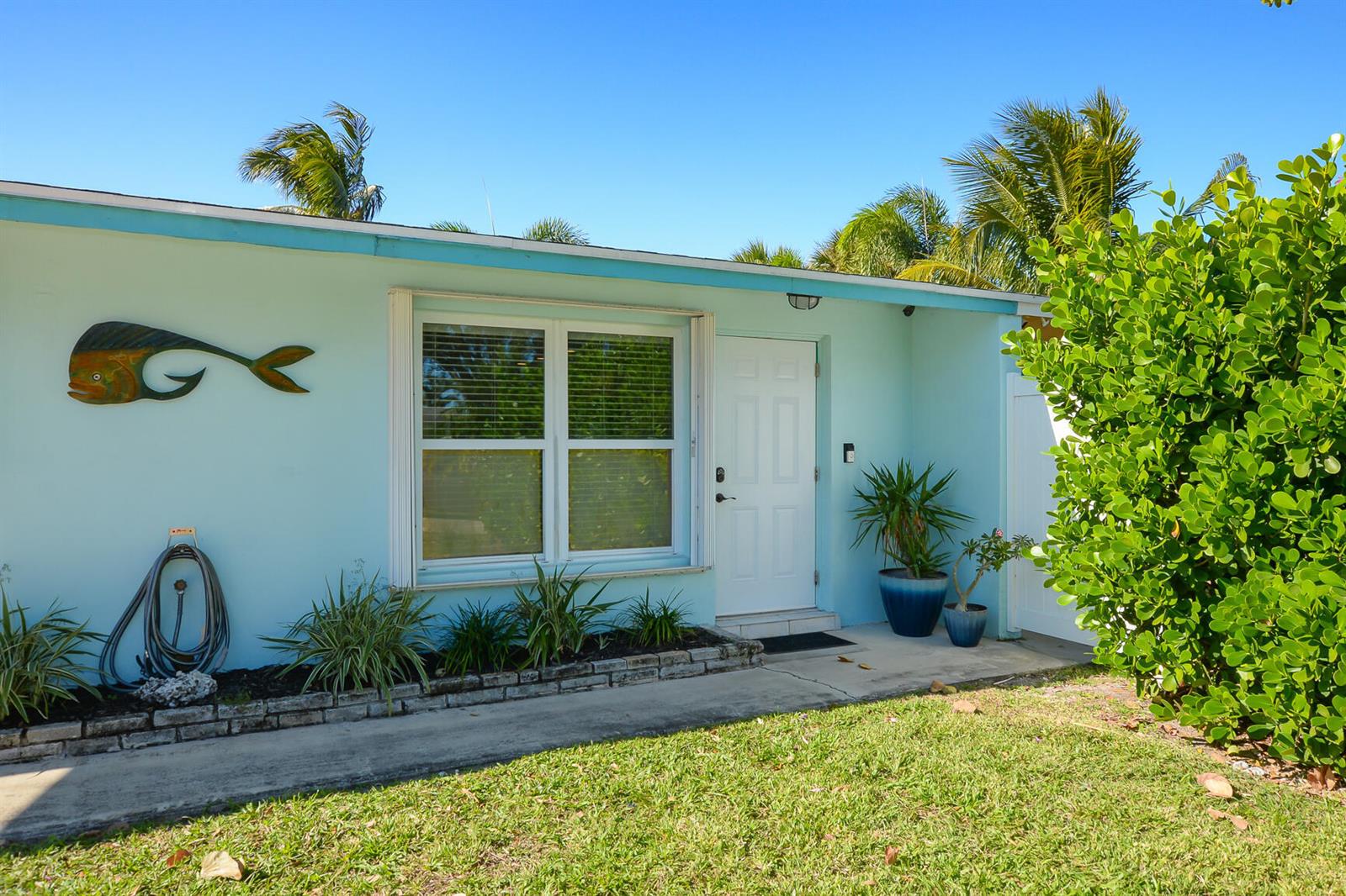 A light blue house exterior features a white front door, a window, and a fish decoration — 110 SW Hideaway Place, Stuart FL 34994, STUART, FL