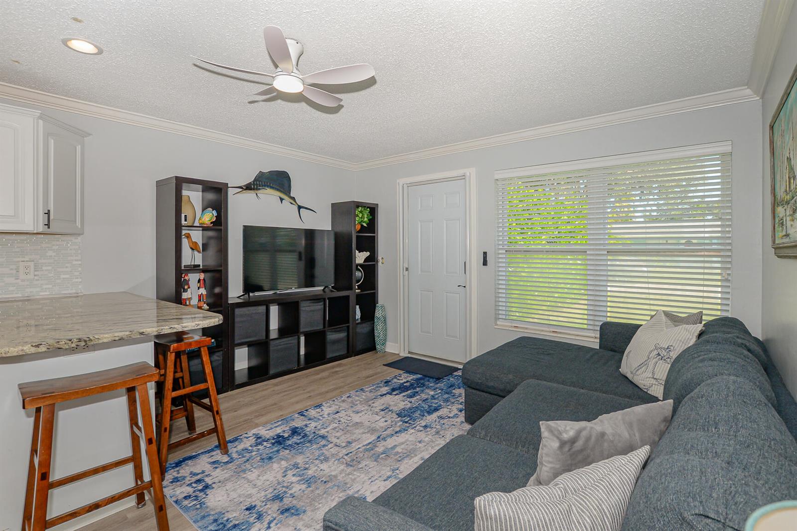 A living room features a blue sectional sofa, a television unit, and a kitchen counter — 110 SW Hideaway Place, Stuart FL 34994, STUART, FL