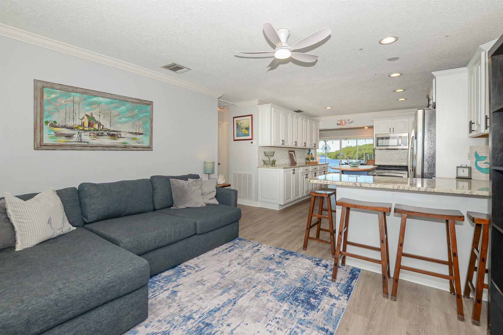 A living room with a blue sectional sofa opens into a kitchen with white cabinets — 110 SW Hideaway Place, Stuart FL 34994, STUART, FL