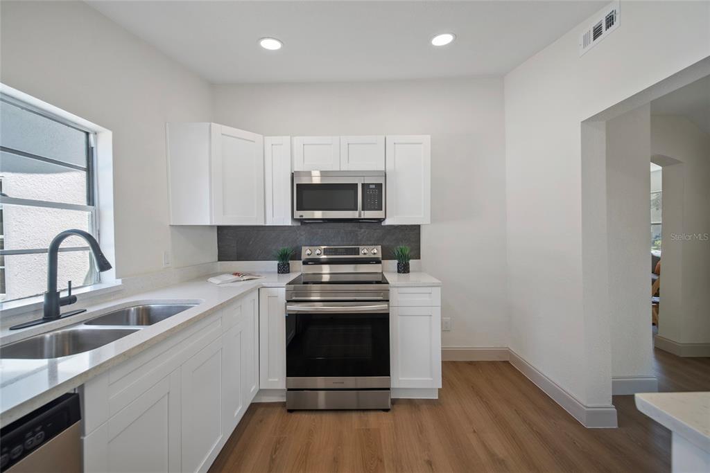 A kitchen features white cabinets, stainless steel appliances, a dark backsplash, and wood-look flooring — 2930 W ARCH STREET, TAMPA, FL