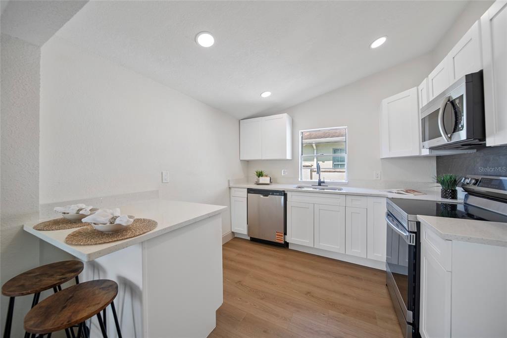 A modern kitchen features white cabinets, stainless steel appliances, and a breakfast bar with stools — 2930 W ARCH STREET, TAMPA, FL