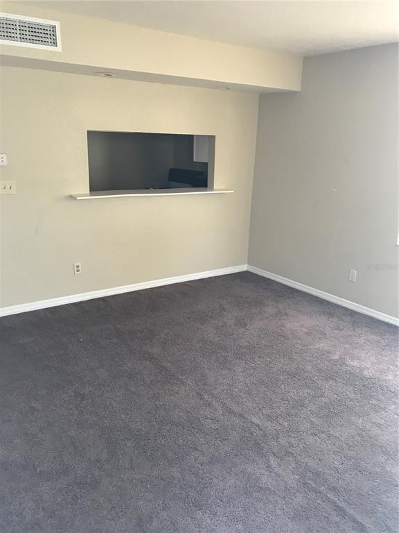 An empty room with grey carpet, beige walls, and a kitchen pass-through window — 7101 E BANK DRIVE UNIT 7101, TAMPA, FL