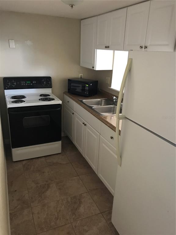 A kitchen features white cabinets, a black stove, a microwave, and a white refrigerator — 7101 E BANK DRIVE UNIT 7101, TAMPA, FL