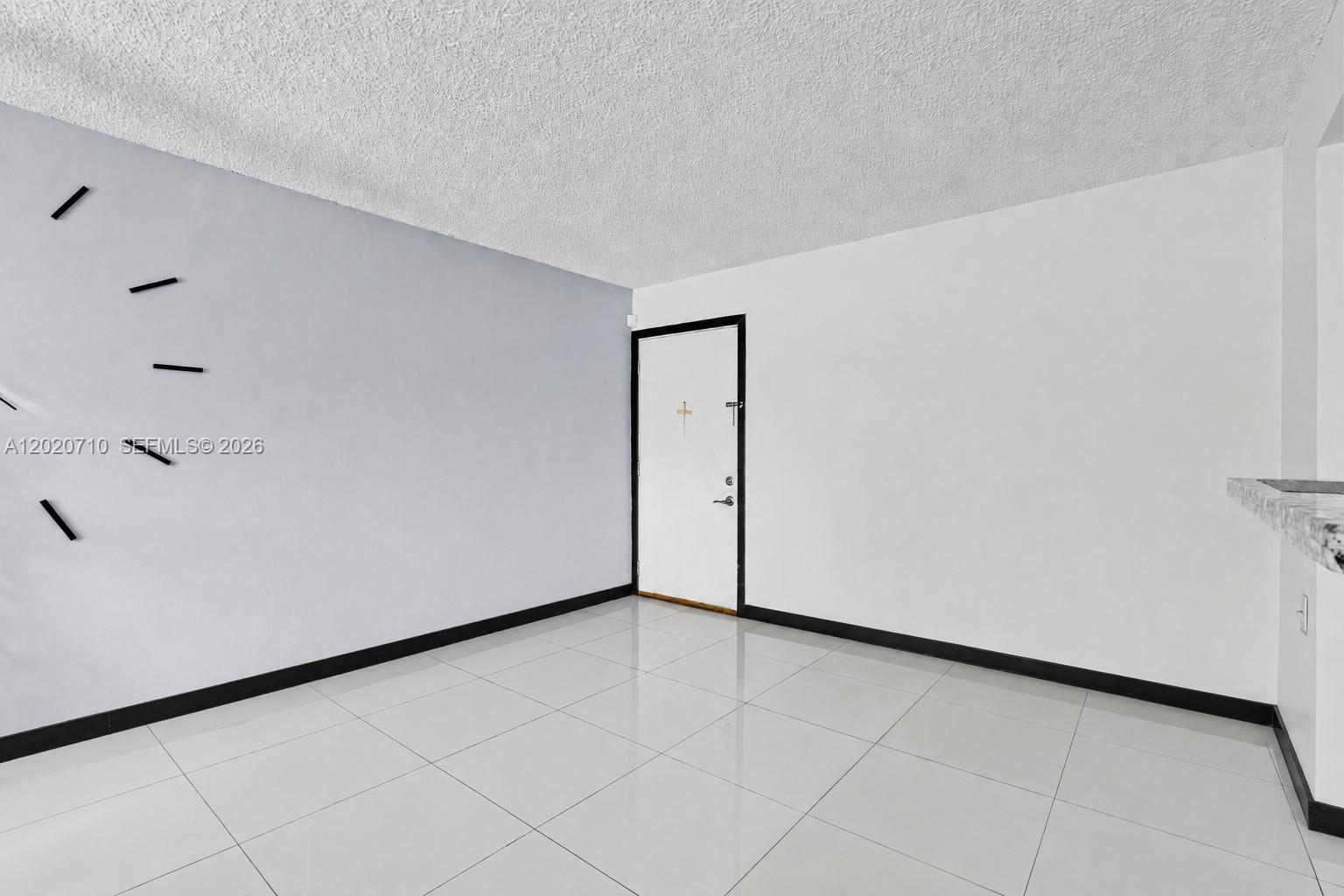 An empty room features white tile flooring, a textured ceiling, and a white entry door — 15430 SW 82nd Ln # 622, Miami FL 33193, MIAMI, FL