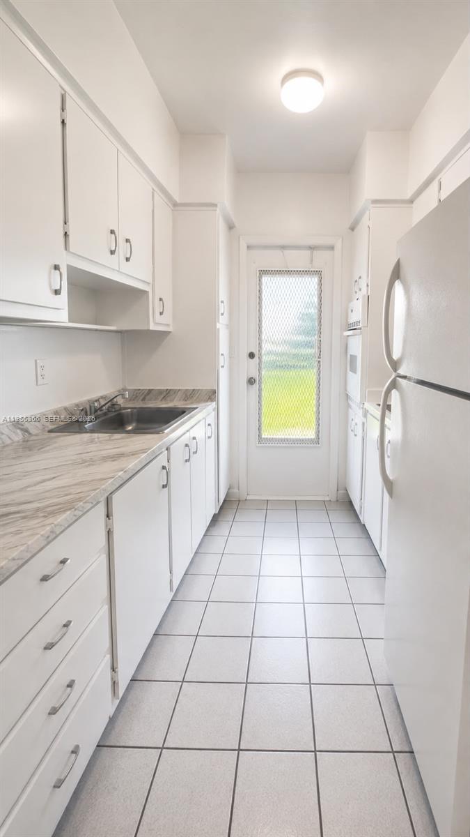 A narrow galley kitchen features white cabinets, marble-patterned countertops, and a glass-paneled exterior door — 12655 NE 16th Ave # 16, North Miami FL 33161, NORTH MIAMI, FL