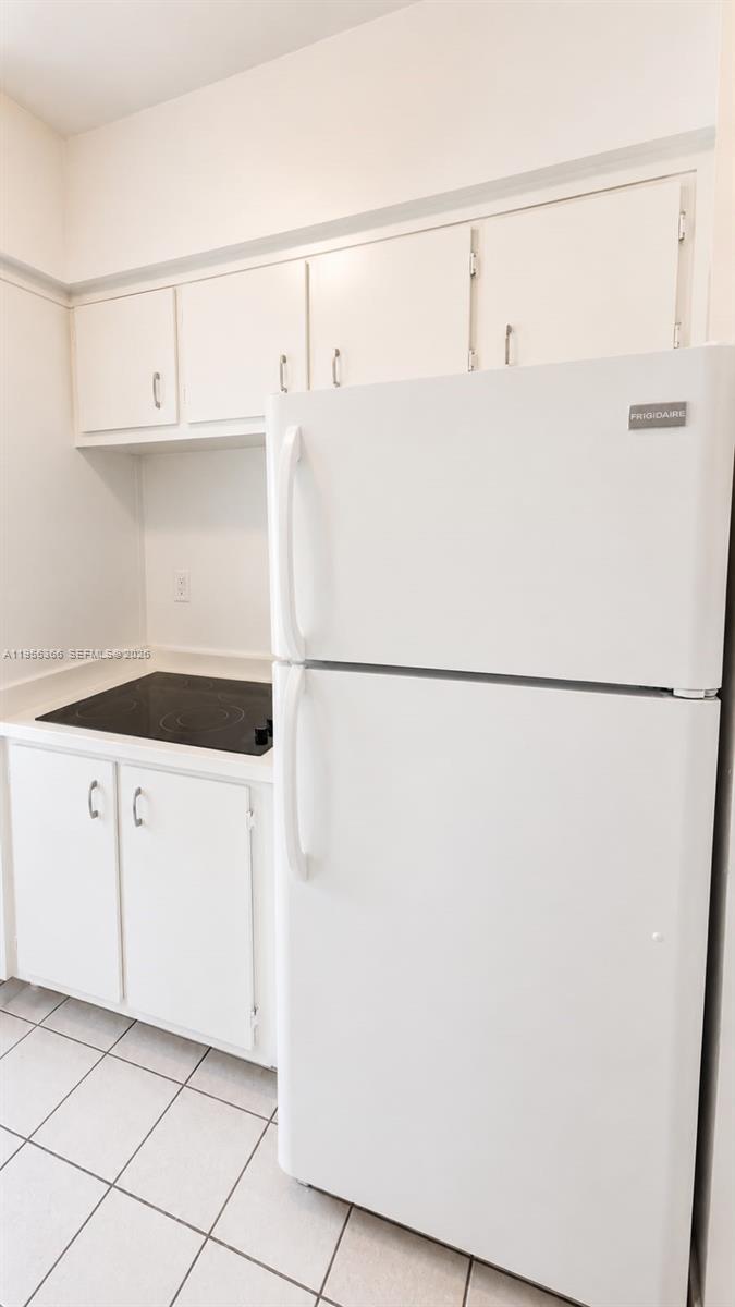 A white kitchen features a Frigidaire refrigerator, a black electric cooktop, and white cabinetry — 12655 NE 16th Ave # 16, North Miami FL 33161, NORTH MIAMI, FL
