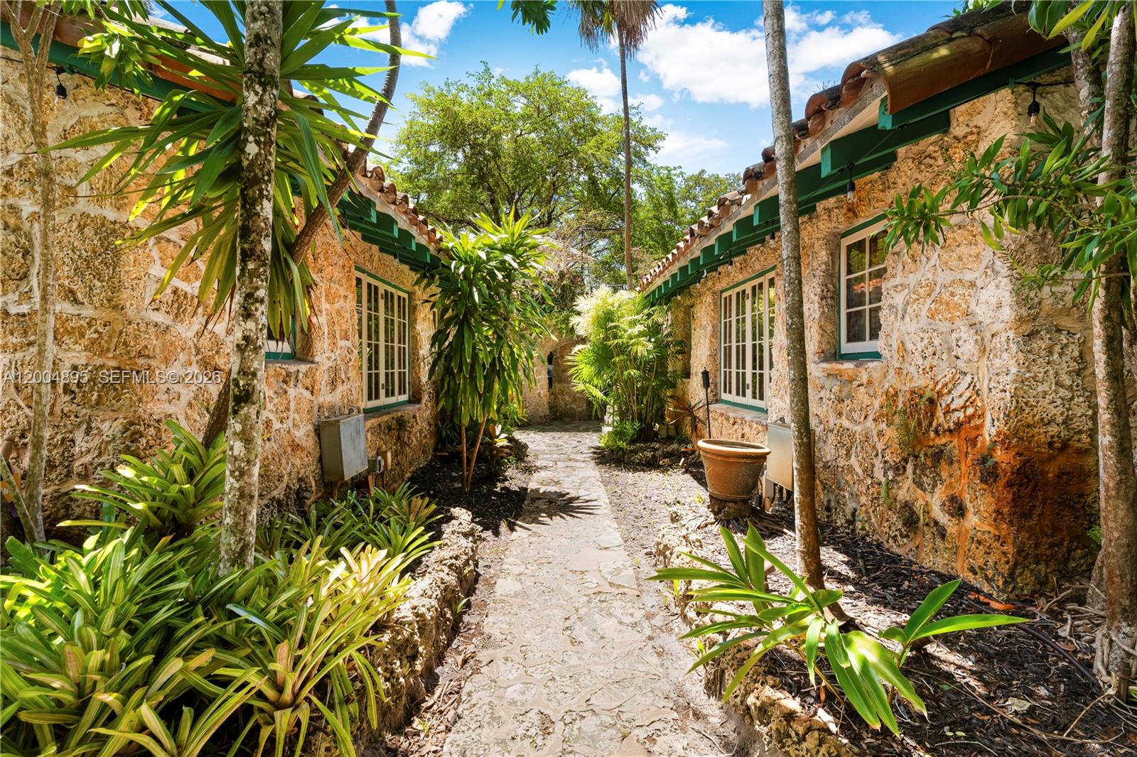 A stone pathway leads between two rustic stone buildings surrounded by lush tropical plants — 1301 Milan Ave, Coral Gables FL 33134, CORAL GABLES, FL