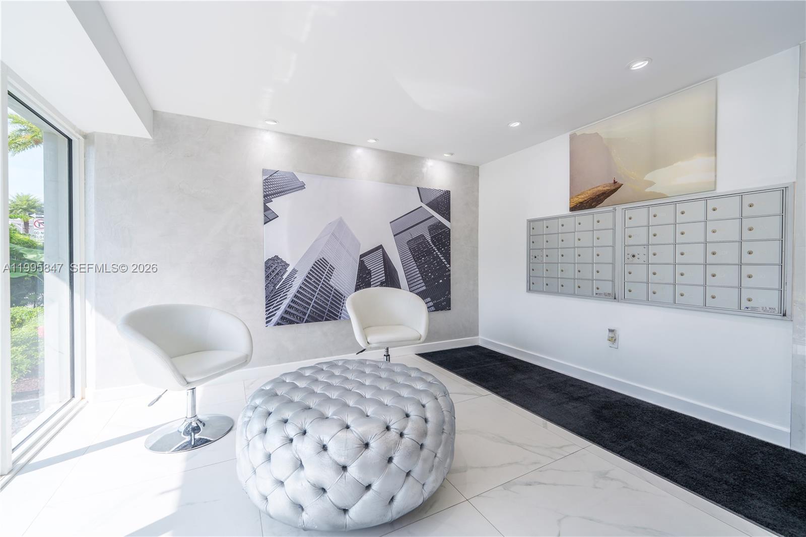 A modern lobby features white chairs, a tufted ottoman, mailboxes, and city-themed wall art — 720 Collins Ave # 506, Miami Beach FL 33139, MIAMI BEACH, FL