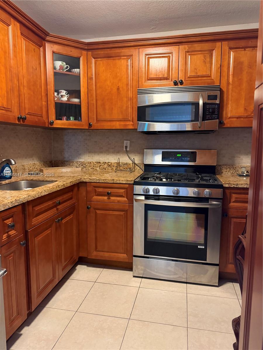 A kitchen features wood cabinets, granite countertops, stainless steel appliances, and light-colored tile flooring — 720 Collins Ave # 506, Miami Beach FL 33139, MIAMI BEACH, FL