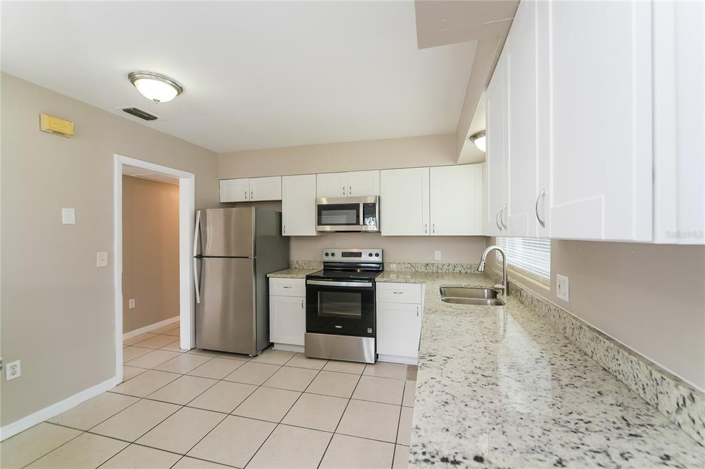 A kitchen features white cabinets, granite countertops, stainless steel appliances, and light-colored tile flooring — 936 ALECON DRIVE, ORLANDO, FL