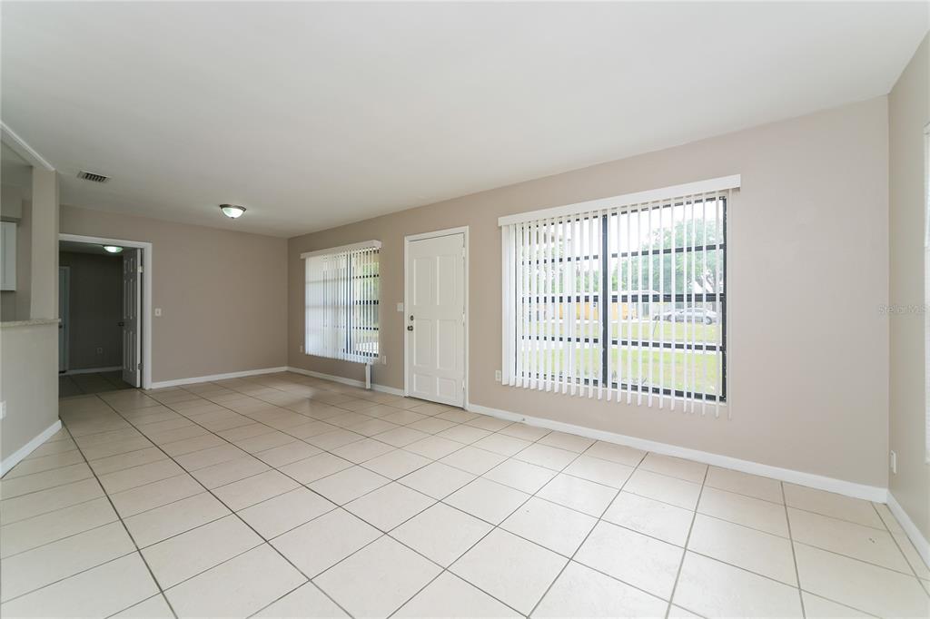 An empty living room features light-colored floor tiles, beige walls, and two large windows — 936 ALECON DRIVE, ORLANDO, FL
