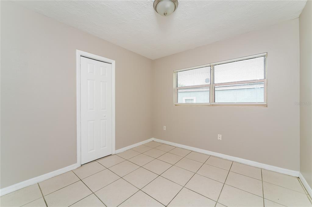 An empty room features beige walls, a white door, a window with blinds, and tiled flooring — 936 ALECON DRIVE, ORLANDO, FL
