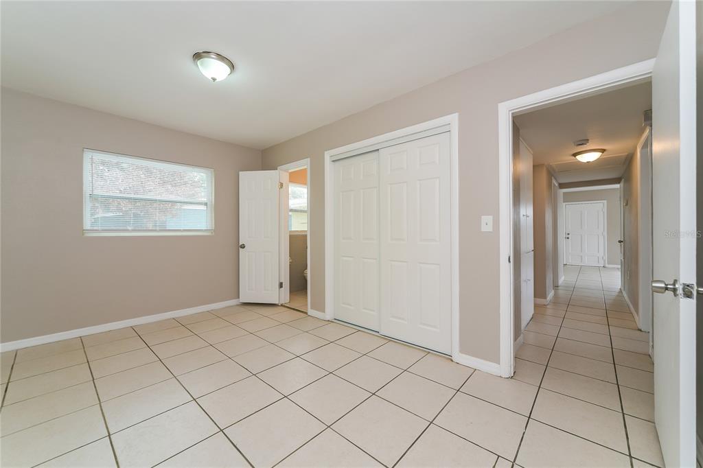 A bedroom with beige walls, tiled floors, a sliding closet, and an attached bathroom — 936 ALECON DRIVE, ORLANDO, FL