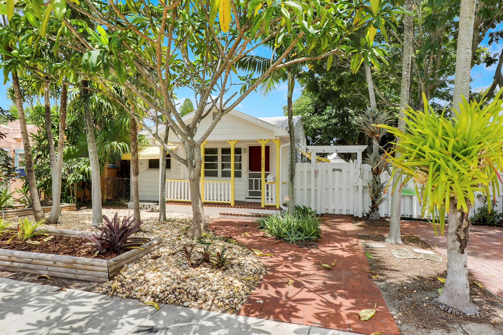 A small white cottage with yellow trim and a brick walkway surrounded by tropical landscaping — 412 N K Street, FL 33460, FL