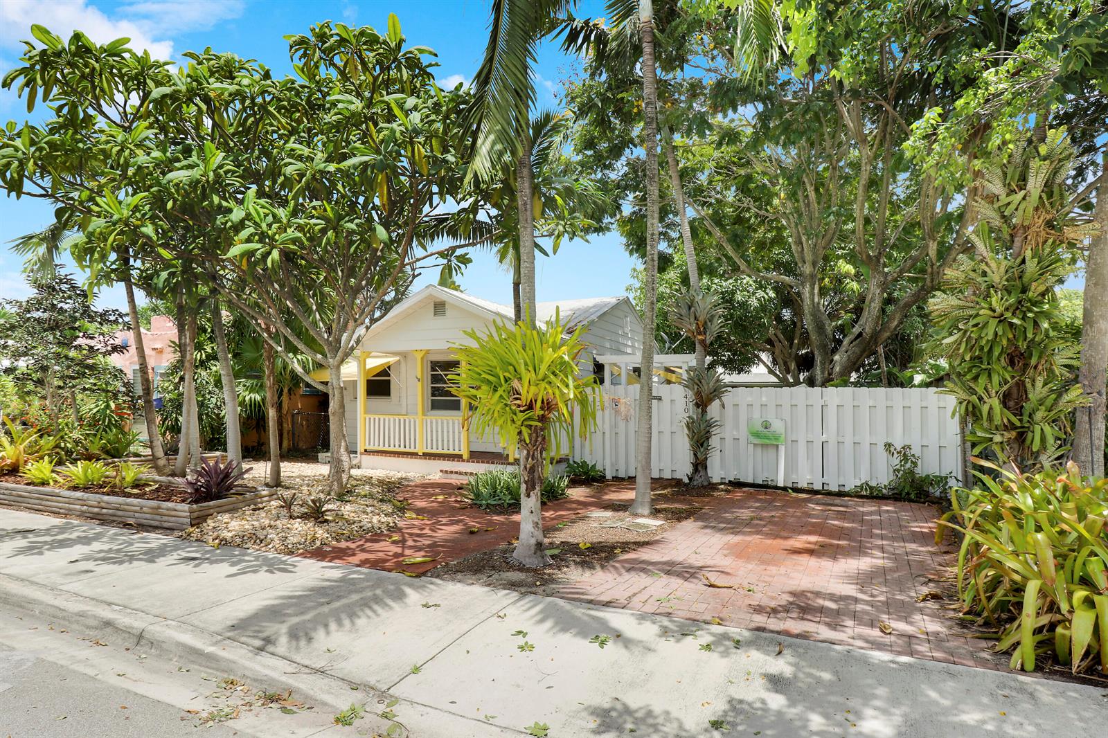 A small white cottage with a yellow porch sits behind a white fence and driveway — 412 N K Street, FL 33460, FL