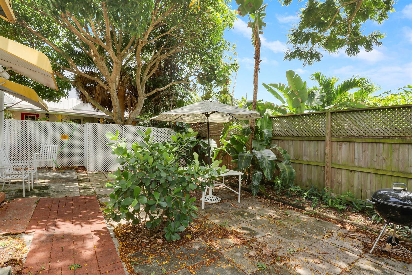 A backyard patio features a brick walkway, a dining table with an umbrella, and fencing — 412 N K Street, FL 33460, FL