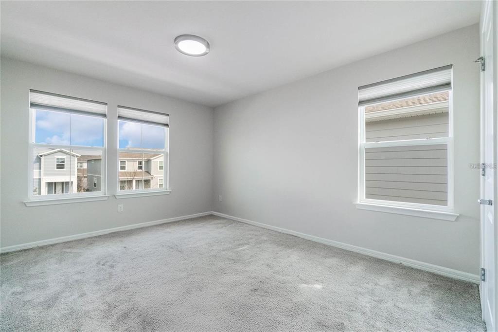 An empty bedroom with gray carpet, light gray walls, and three windows — 14218 LANIKAI BEACH DRIVE, ORLANDO, FL