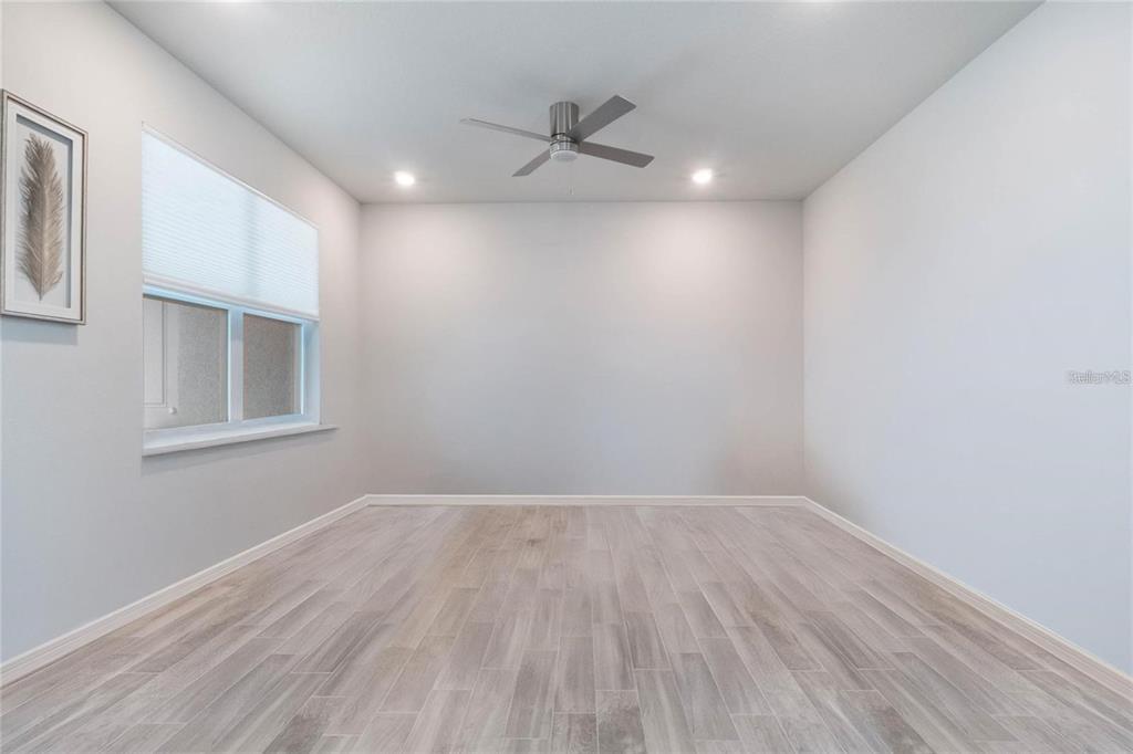 A bright, empty room features light wood-look tile flooring, a ceiling fan, and a window — 14218 LANIKAI BEACH DRIVE, ORLANDO, FL