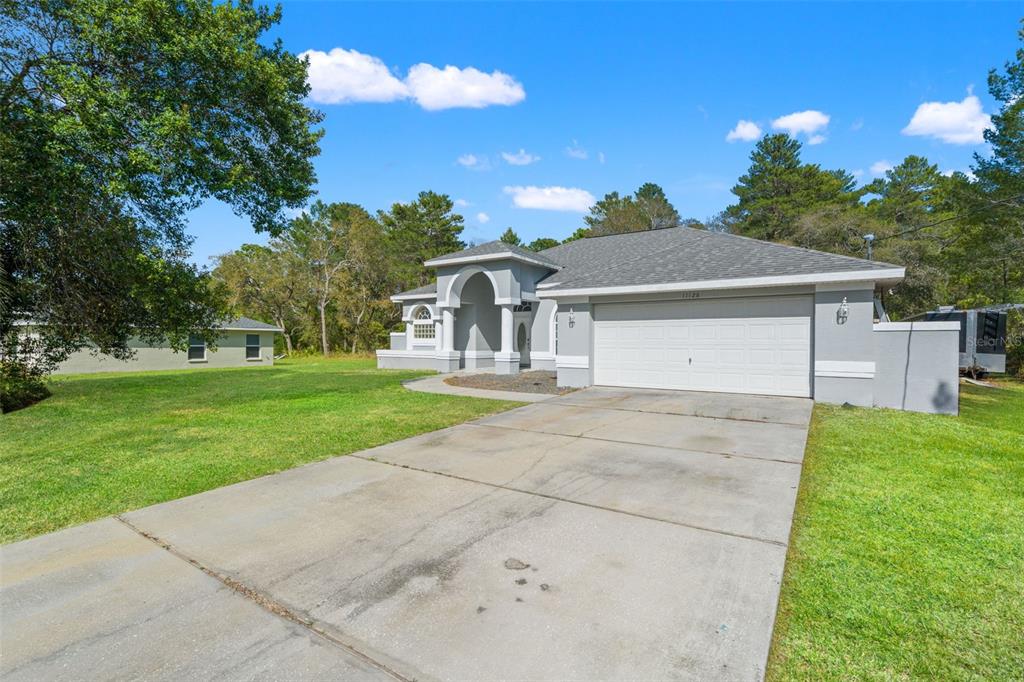 A gray single-story house with a two-car garage and an arched entryway sits on a lawn — 11128 LOMITA WREN ROAD, WEEKI WACHEE, FL