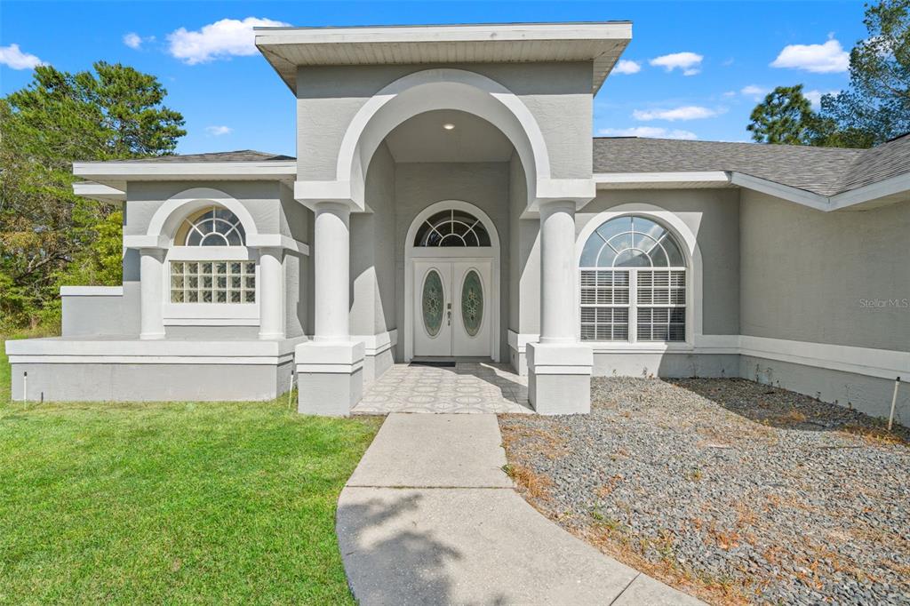 The exterior of a gray house features a covered entryway with white columns and arches — 11128 LOMITA WREN ROAD, WEEKI WACHEE, FL
