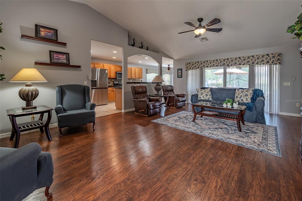 A living room with wood flooring, a vaulted ceiling, and an open view into the kitchen — 1708 SW 155TH PLACE ROAD, OCALA, FL